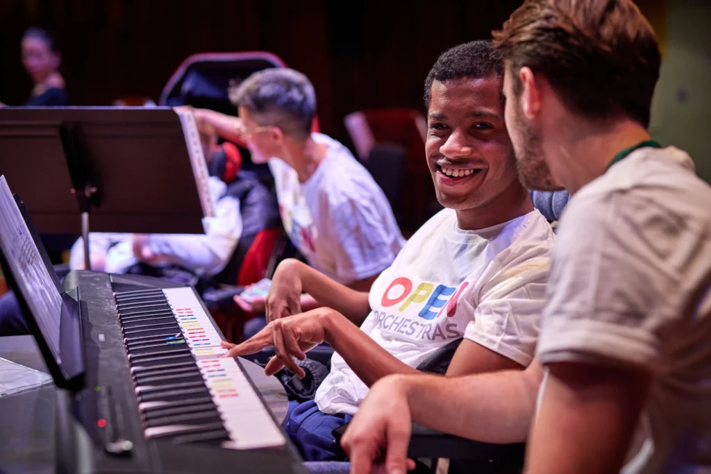 Picture of a smiling young musician playing keyboard with a teacher by his side